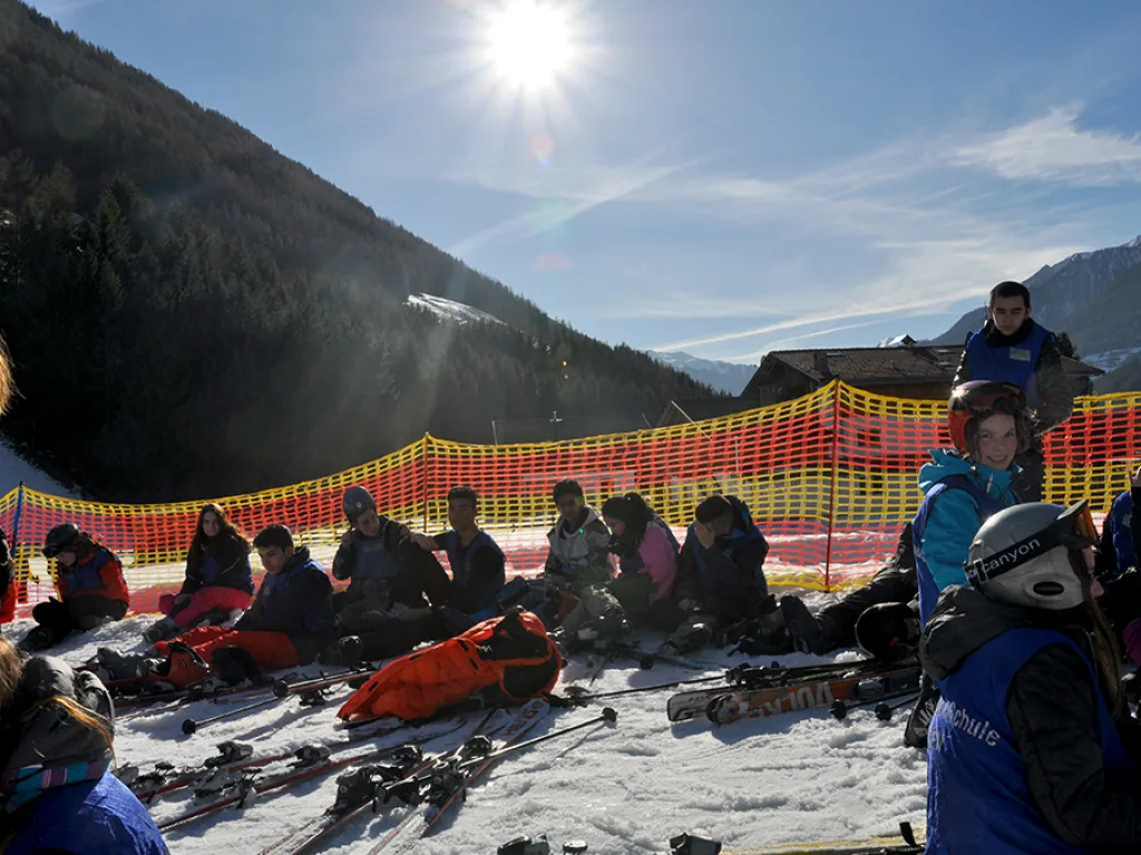 Ausrüstung liegt im Schnee, dahinter sitzen Jugendliche gegen die Sonne.